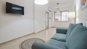 Ett vardagsrum med en platt-TV som är monterad på väggen, en blå soffa, en mönstrad matta och ett fönster med utsikt över omgivningen.