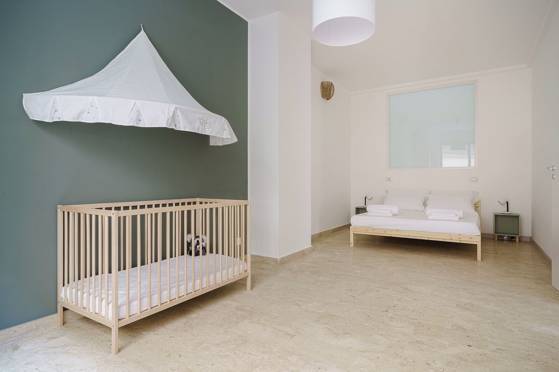 Ein Zimmer mit einem Babybett, einem Bett, einem Fenster und einem wandmontierten Baldachin.