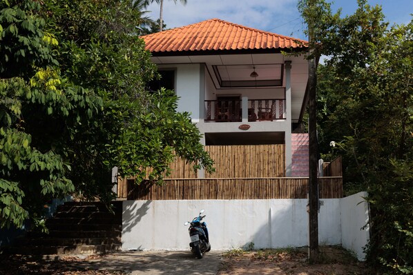 A two-story house with a red-tiled roof, a balcony, and a white wall.