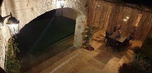 Zona de piscina exterior con paredes de piedra, una mesa y sillas, y un farol.