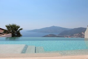 Una piscina infinita de color azul intenso con vistas al mar y montañas lejanas.