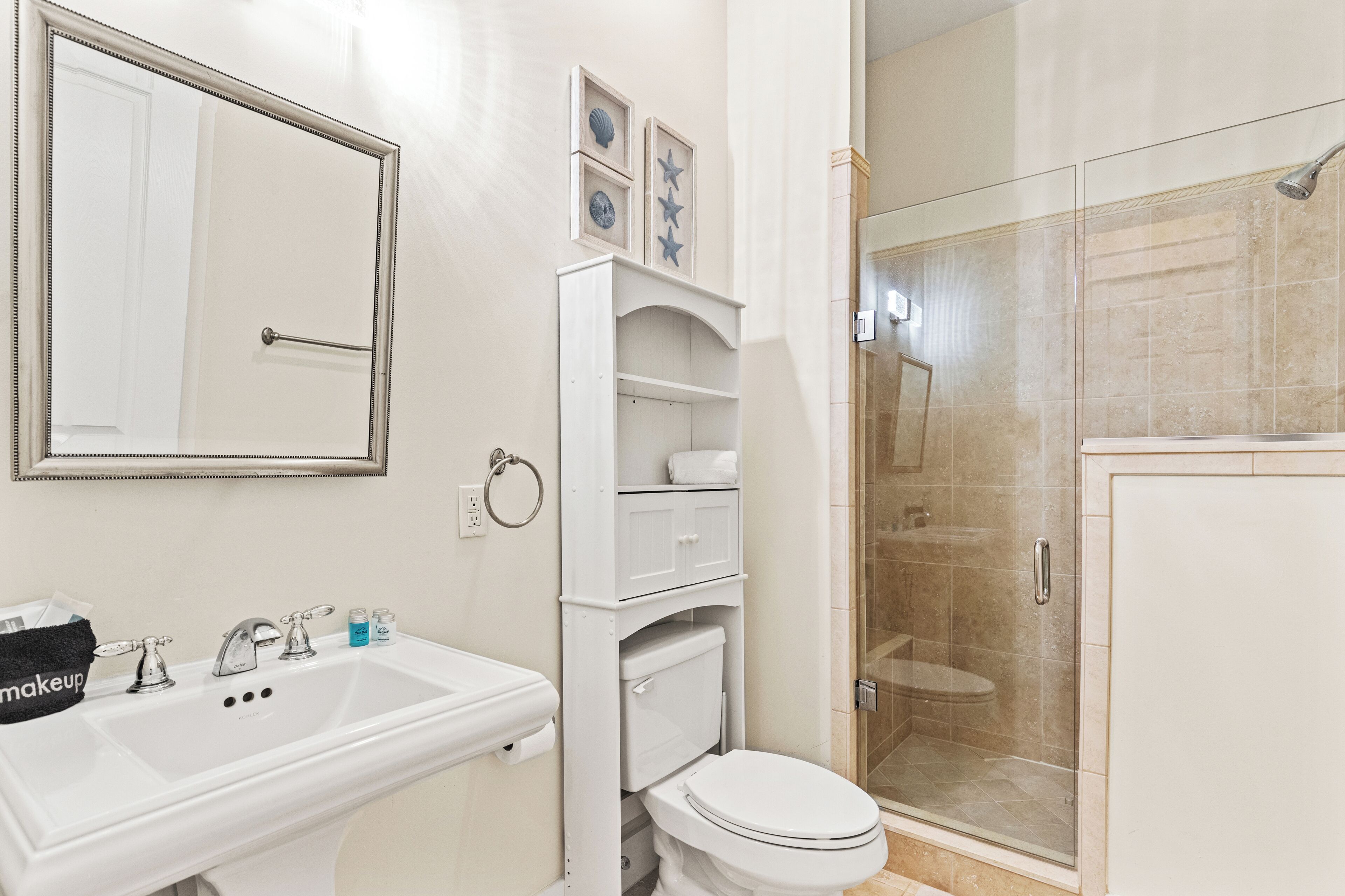 Un baño con lavamanos blanco, espejo, inodoro y cabina de ducha con paredes de vidrio.
