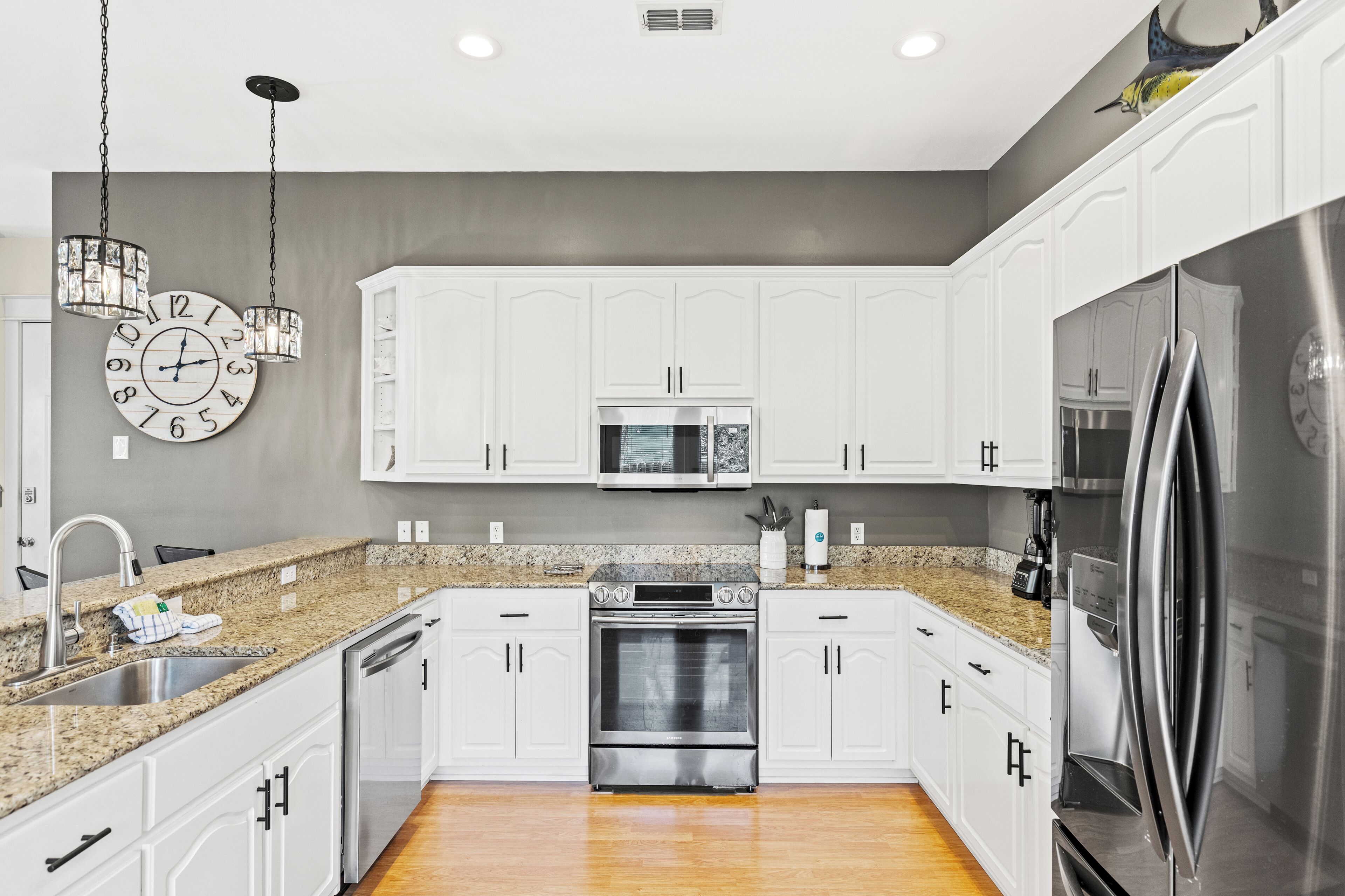 A modern kitchen with white cabinets, a granite countertop, stainless steel appliances, and a wall clock.