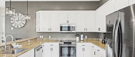 A modern kitchen with white cabinets, a granite countertop, stainless steel appliances, and a wall clock.