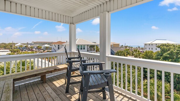 A covered outdoor area with a wooden deck, white railing, and two Adirondack chairs. - Beach House Spacious 4BR Retreat With Gulf Views & Observation Deck! (Panama City Beach)
