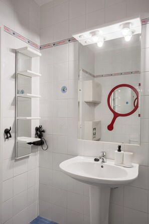 A bathroom with a white sink, a mirror with a red frame, and a shelf with toiletries.