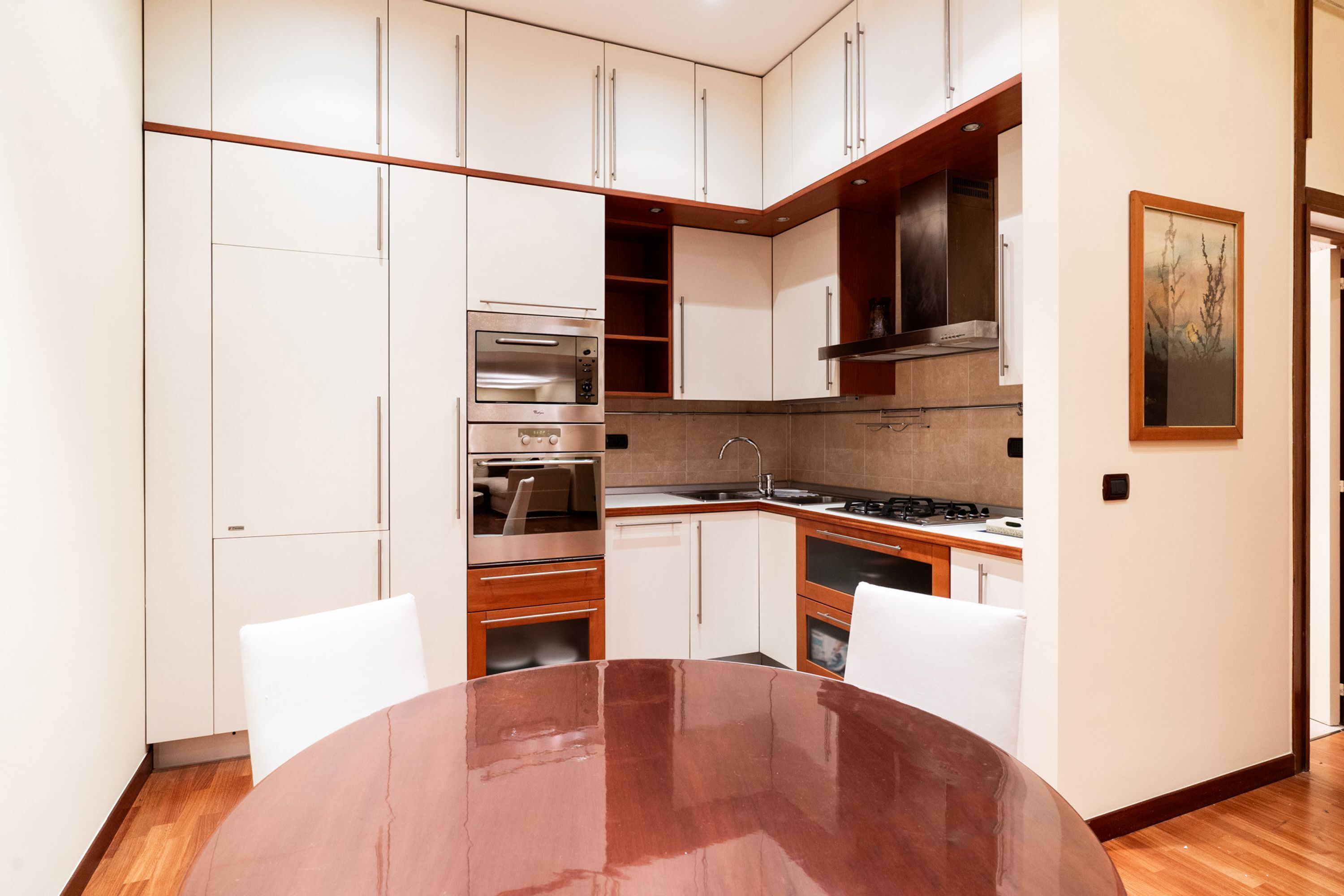 A modern kitchen with white cabinets, a built-in oven, a stove, and a dining table with chairs. - Umbertina Cozy Apartment by Wonderful Italy (Bari)