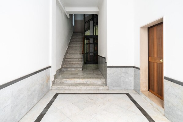 A staircase leading to a wooden door, with a tiled floor and a white wall.