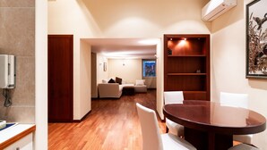 A modern dining area with a wooden table and white chairs, a wooden floor, and a view into a living room with a sofa and a painting. - Umbertina Cozy Apartment by Wonderful Italy (Bari)