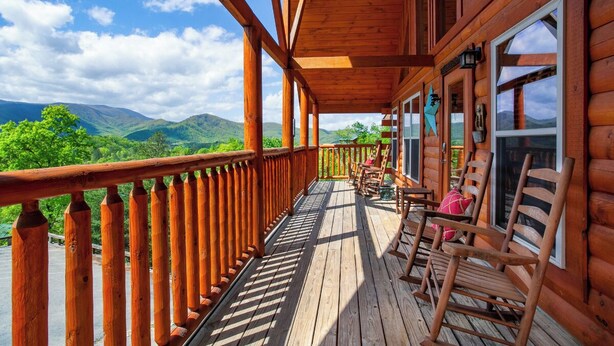 Een houten terras met uitzicht op bergen, houten stoelen en een hekwerk.