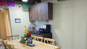 A dining area with a wooden table and chairs, a kitchen in the background, and decorative paper banners.