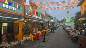 A street lined with colorful buildings, including a hostel and a Mexican restaurant. There are tables and chairs outside the businesses, and a motorcycle is parked on the side.
