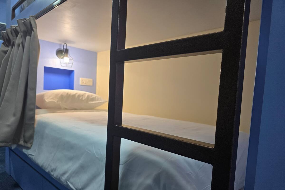 Una cama individual con cortina a la izquierda, una luz fijada a la pared y una pared de acento azul.