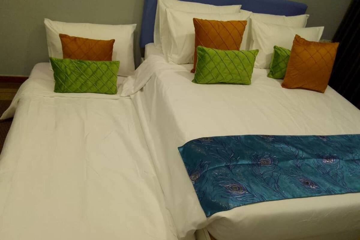 Cama doble con ropa de cama blanca y varios cojines en tonos verde y naranja.