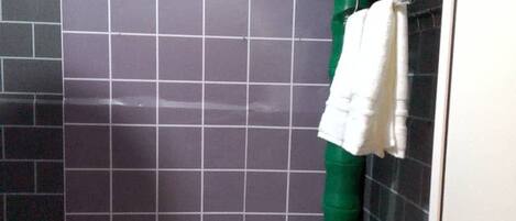Un bagno piccolo con un lavandino bianco, pareti piastrellate scure e un portaserviti verde.