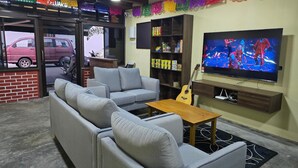 A living room with grey sofas, a wooden coffee table, a guitar, a TV on the wall, and colorful paper decorations.