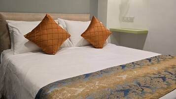 Un lit bien fait, agrémenté d’oreillers blancs et orange, d’une couvre-lit bleue et dorée à motifs, et d’une petite lampe de chevet fixée au mur.