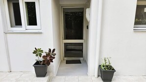 A clean, white exterior of a building with a narrow entrance and two potted plants on either side. - Travelers Nest by Checkin (Heraklion)