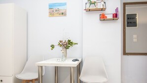 A small, clean room with a white table, two white chairs, a vase with dried plants, and a painting on the wall. - Travelers Nest by Checkin (Heraklion)