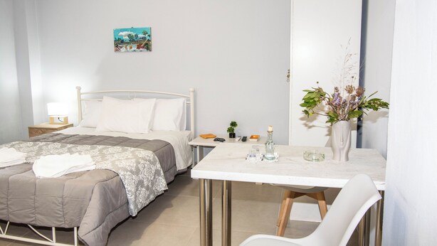 A bedroom with a bed, bedside table, and a desk with a chair. - Travelers Nest by Checkin (Heraklion)