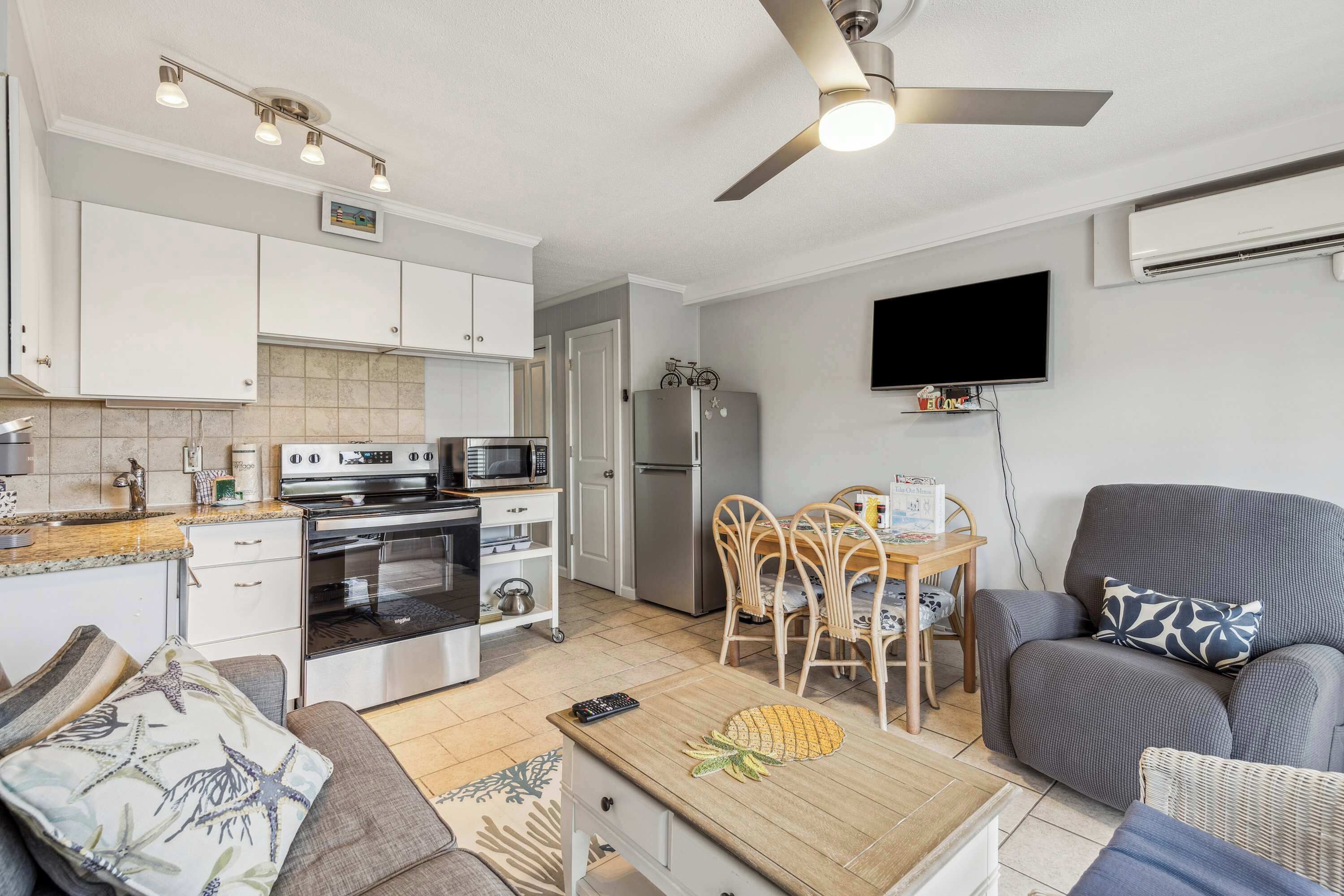 A compact living space with a kitchenette, a dining area, a sofa, and a flat-screen TV mounted on the wall.