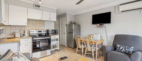 A compact living space with a kitchenette, a dining area, a sofa, and a flat-screen TV mounted on the wall.
