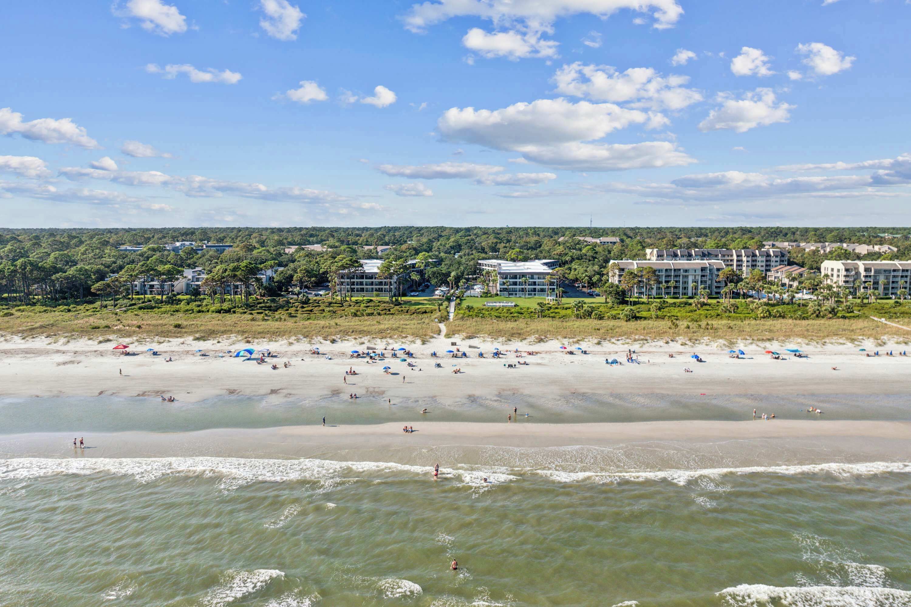 Ein Strand mit einem Hotel im Hintergrund, sandigem Ufer und dem Ozean.