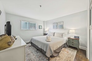A bedroom with a bed, bedside tables, a lamp, a TV, and a decorative fish on a dresser.