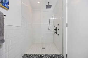 A walk-in shower with white tiled walls, a showerhead, and a control panel. - Stylish Group Retreat –Sleeps 16 (New York)