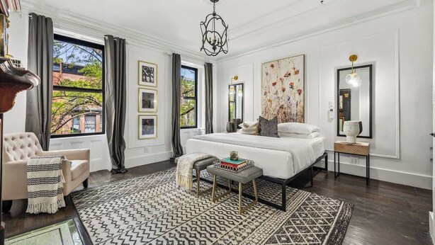 A bedroom with a large bed, a chair, a small table, and a large window.