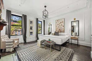 Een slaapkamer met een groot bed, een stoel, een tafeltje en een groot raam.