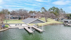 A lakeside property with a dock, a covered seating area, and a house in the background. - Lakefront Family Home for 12, w Picturesque Views (Granite Shoals)