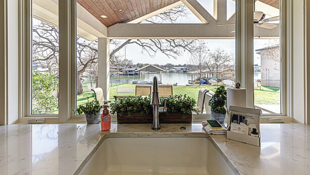 A kitchen with a sink, a wooden ceiling, and a view of a lake and houses. - Lakefront Family Home for 12, w Picturesque Views (Granite Shoals)