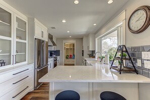 A modern kitchen with white cabinetry, a central island, stainless steel appliances, and a clock on the wall.