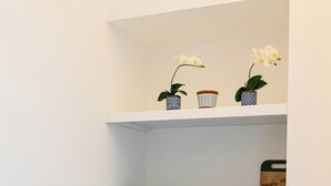 Ett kompakt kök med en diskho, en inbyggd spis och hyllor ovanför för förvaring av skålar och en skärbräda.