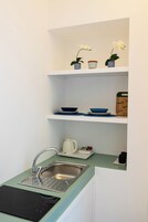 Una cocina compacta con un fregadero, una estufa empotrada y estantes superiores con cuencos y una tabla de cortar.