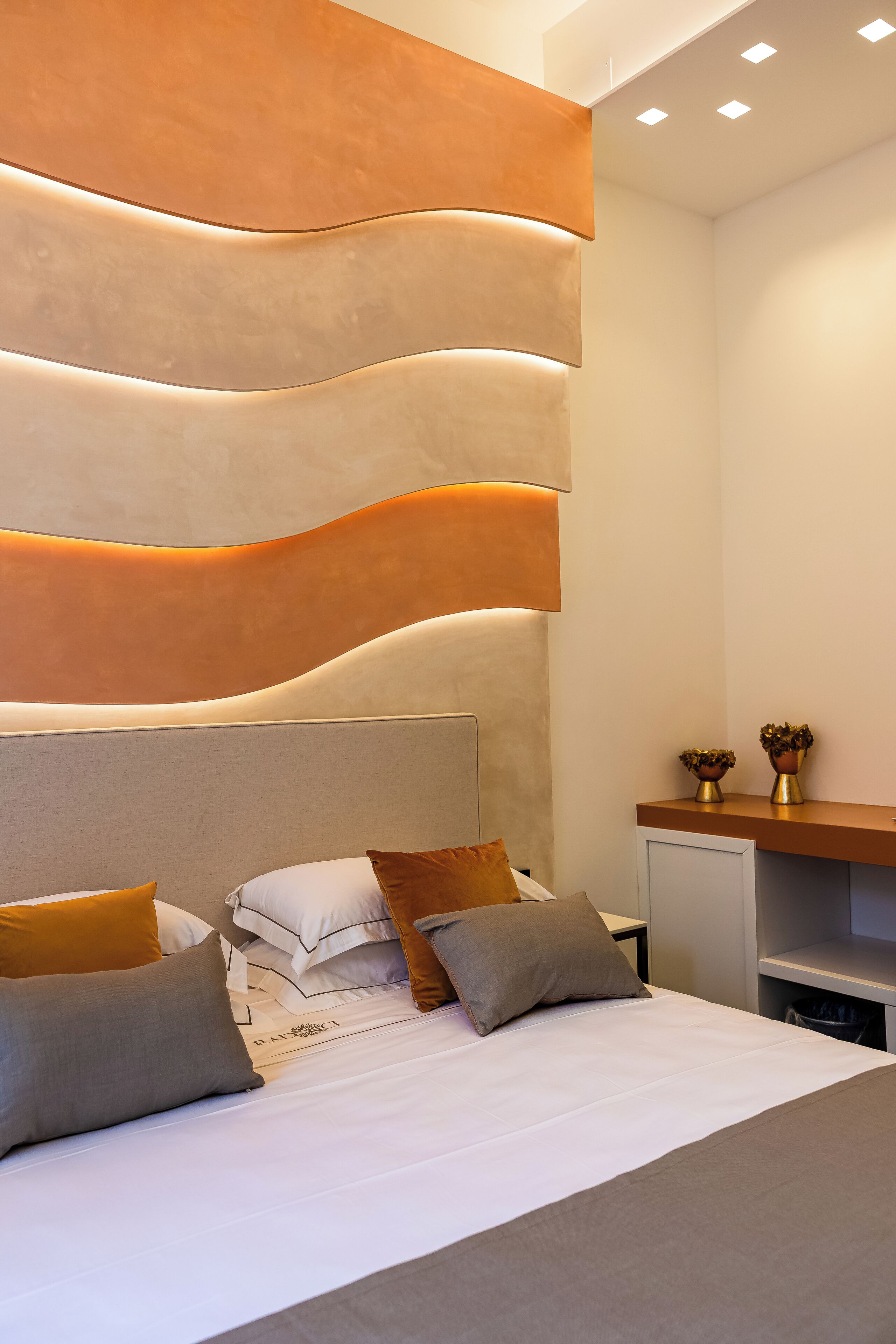 A modern bedroom with a large bed, a headboard with integrated lighting, and a small bedside table with decorative items.