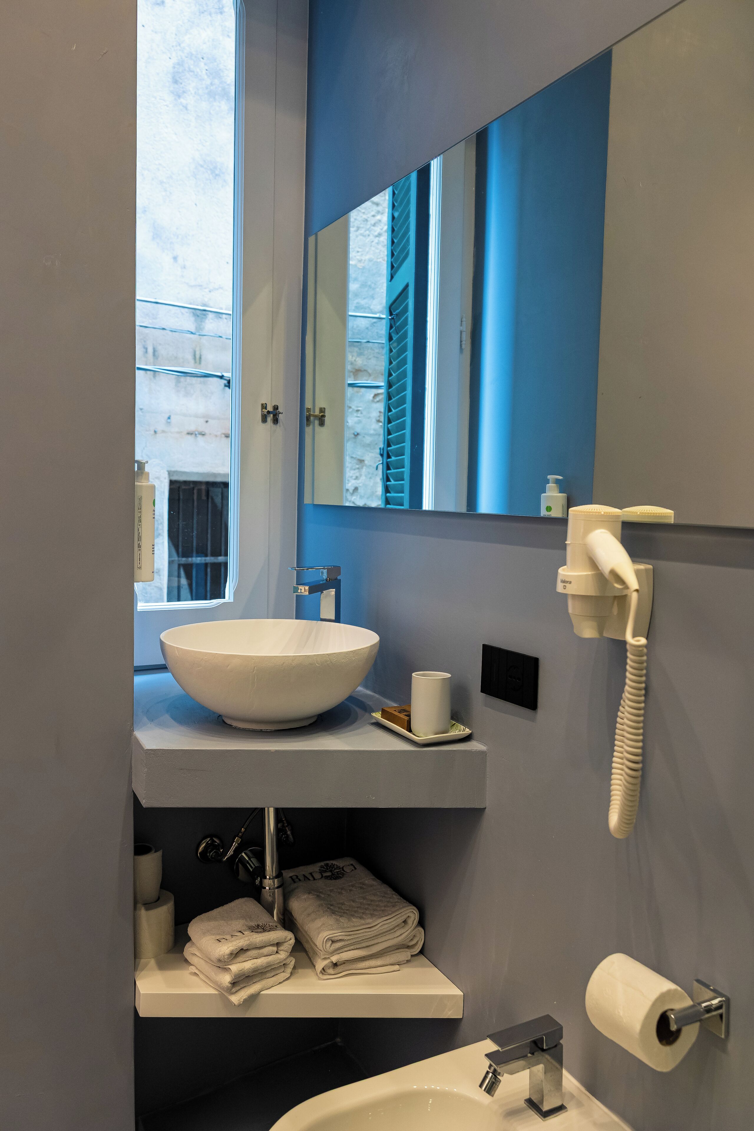A bathroom with a large white sink, a mirror, a telephone, and towels.