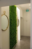 A hallway with a green vertical garden wall, two round mirrors, a white door, and a white wardrobe.