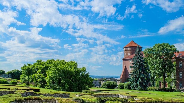 A historic building with a prominent tower, surrounded by lush greenery and a clear blue sky. - Urban Krakow Escape: Balcony, Quiet Retreat & City Center Access (Kraków)