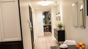 A hallway leading to a dining area with a table set for two, a potted plant, and a fruit bowl on the table. - Urban Krakow Escape: Balcony, Quiet Retreat & City Center Access (Kraków)