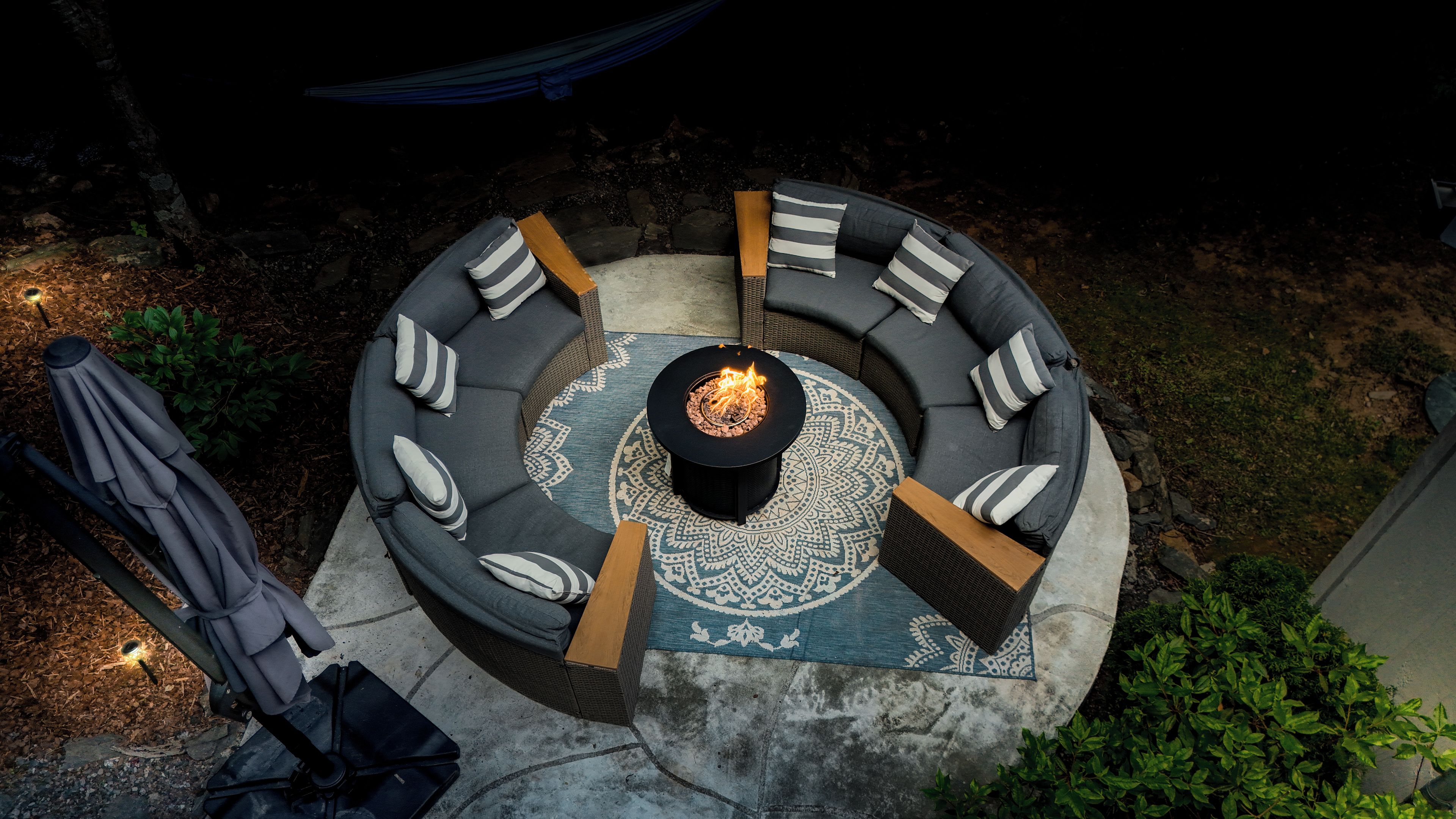 An outdoor seating area with a circular arrangement of sofas and a central fire feature.