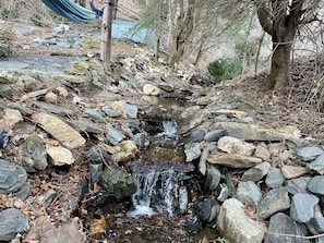 A small waterfall surrounded by rocks and trees in a natural setting. - Cozy Cottage in Todd - Hot Tub, Outdoor Oasis (Todd)