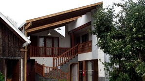 A two-story building with a wooden staircase, a covered balcony, and a small garden area. - Hostal & Cabañas Don Juan (Villarrica)