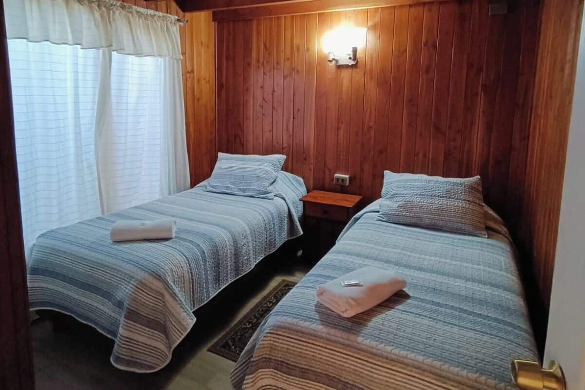 Een kamer met twee bedden, houten wanden, een nachtkastje en een wandlamp.