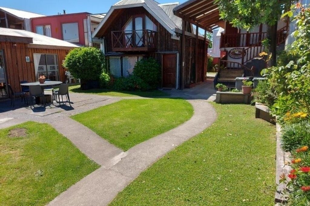 Un edificio de madera con balcón, un patio empedrado y un pequeño espacio al aire libre con sillas y una mesa.