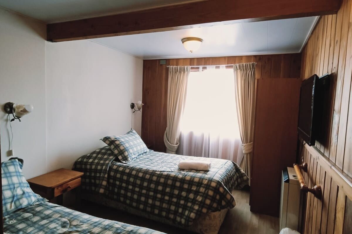 Une chambre avec deux lits, un plafond en bois, une télévision et une fenêtre avec des rideaux.