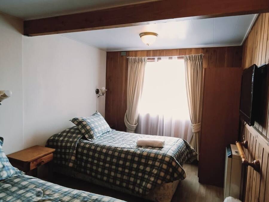 Une chambre avec deux lits, un plafond en bois, une télévision et une fenêtre avec des rideaux.