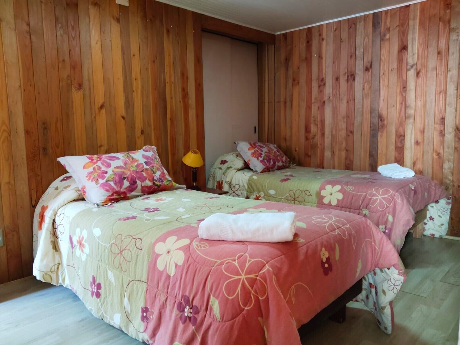 Una habitación con dos camas, paredes de madera y una puerta.