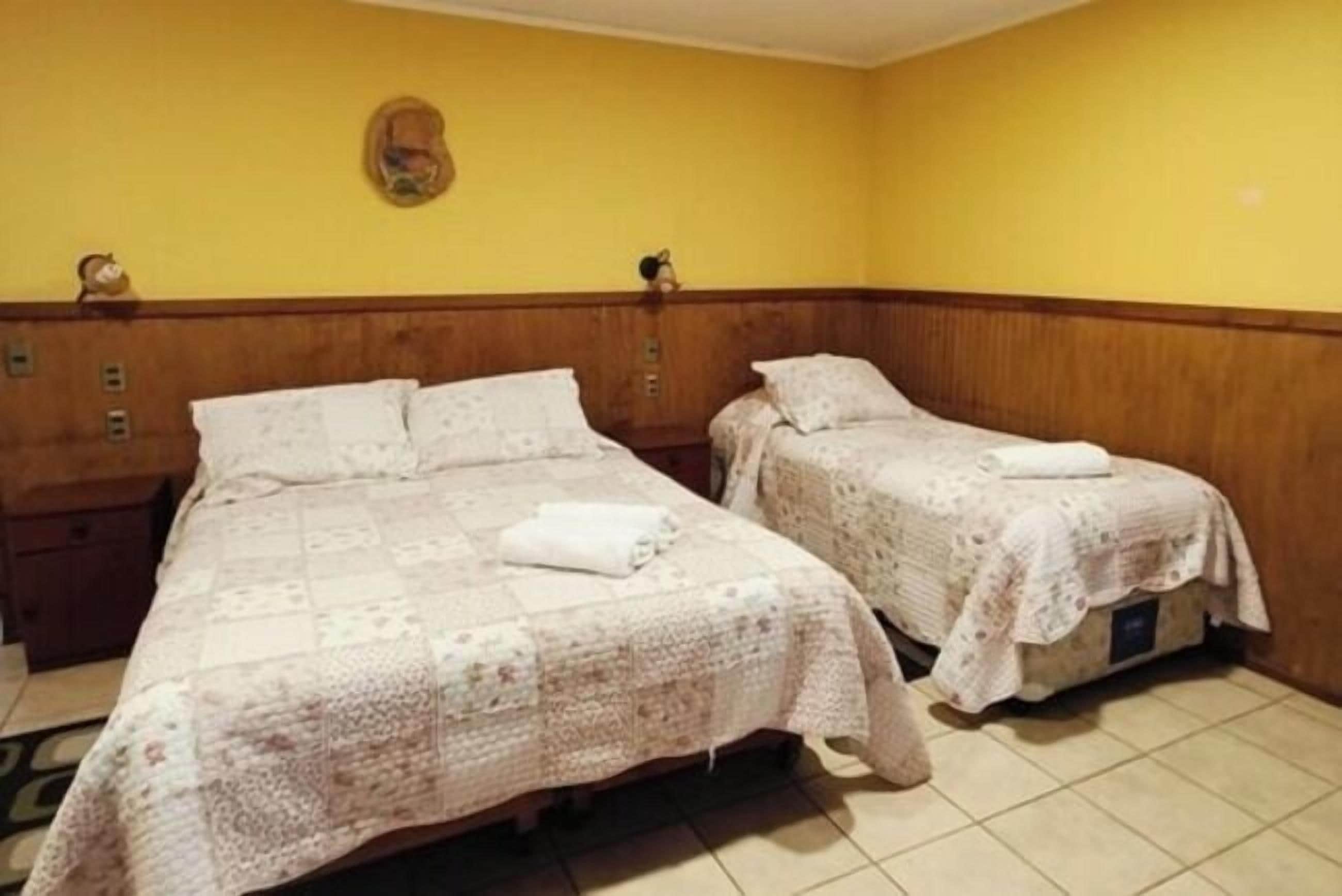 A room with two beds, each with a quilted bedspread and pillows, a wooden headboard, and a wall-mounted clock.